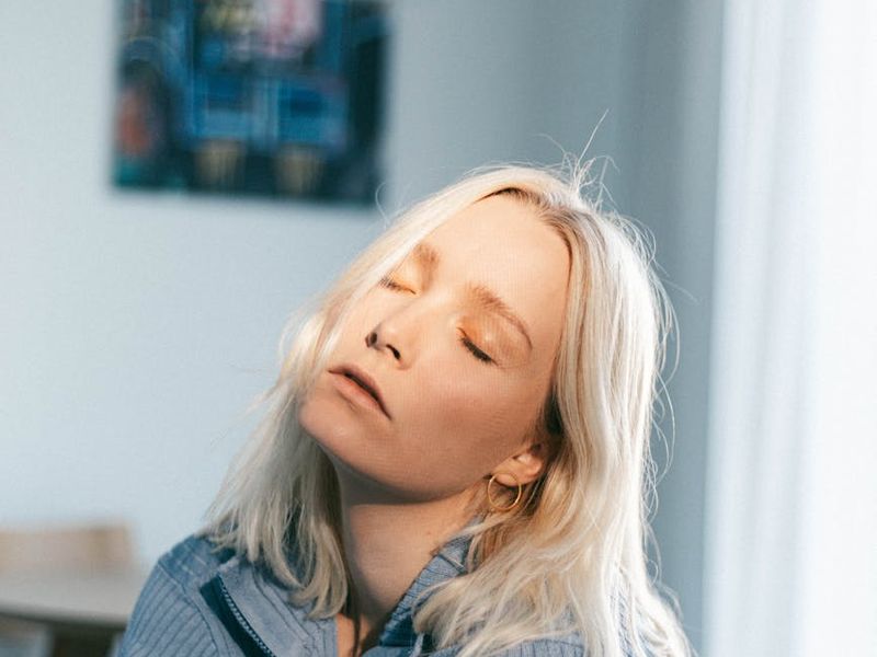 Woman sitting peacefully in a bright room with eyes closed.